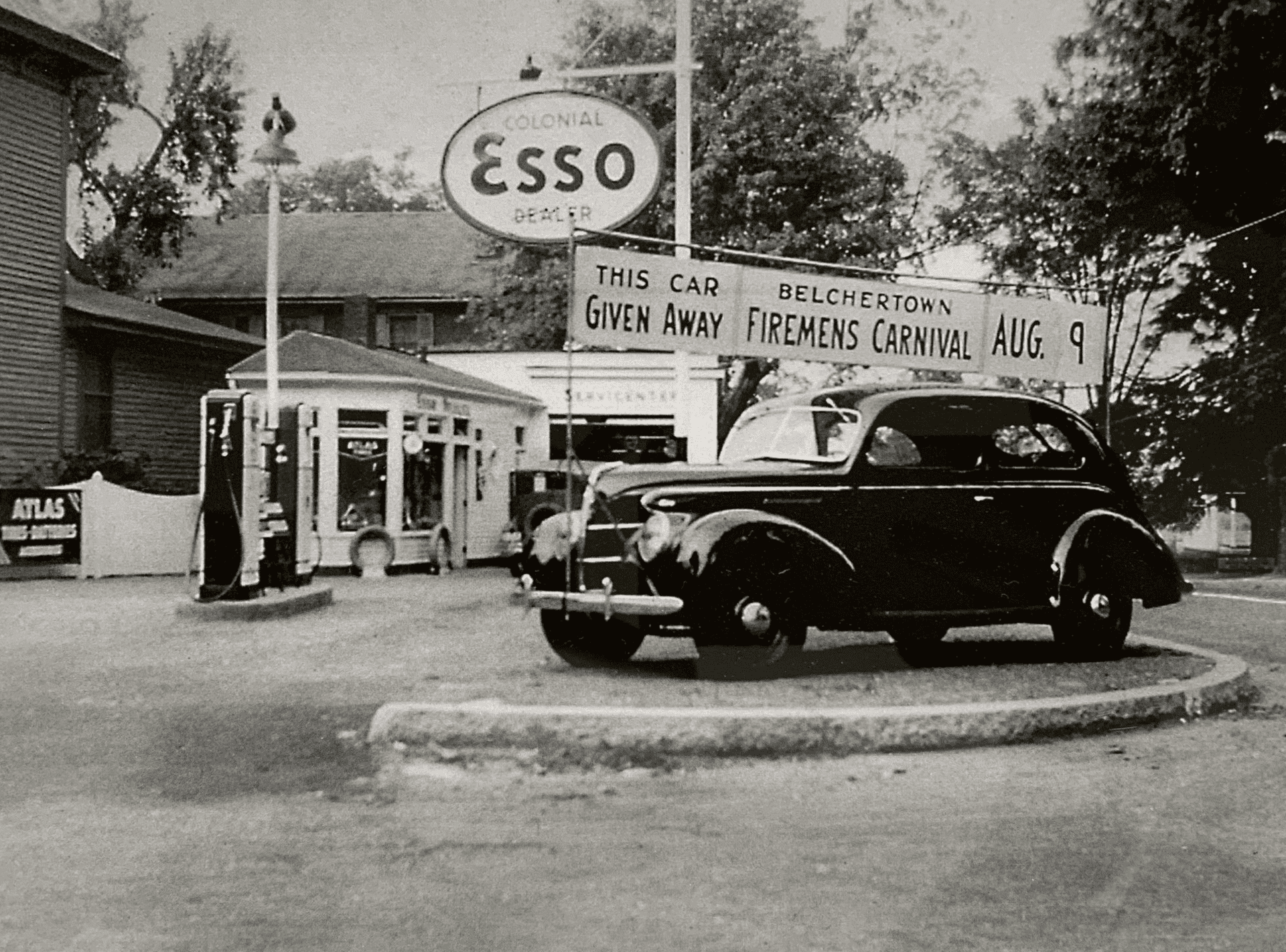 Vintage car parked at an Esso gas station advertising a carnival giveaway on August 9.